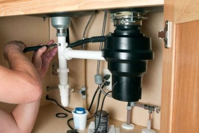 Plumber repairing a garbage disposal beneath a kitchen sink in Atlanta