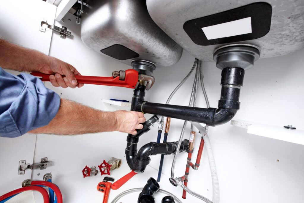 Plumber repairing drain pipes beneath a kitchen sink in Atlanta
